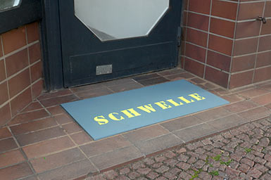 Statt Fußabstreifer eine Holzplatte mit dem Wort Schwelle vor der Galerie