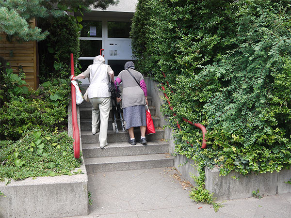 2 alte Damen mit Rollator und Einkaufstüten kämpfen sich eine Treppe hoch